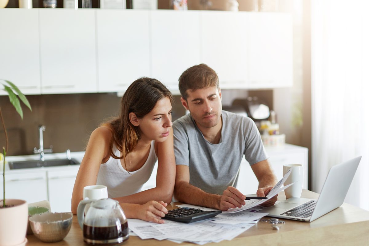Jeune couple vérifiant son budget familial avec une calculatrice avant un achat dans le neuf